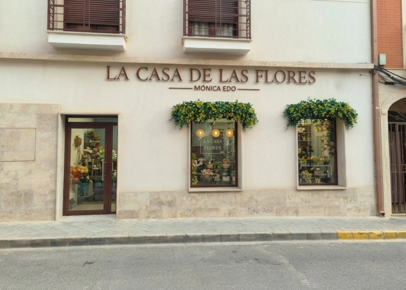 Fachada exterior de la floristería La Casa de las Flores con escaparates decorados y puerta de acceso.